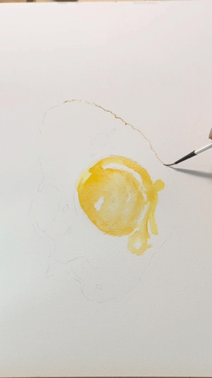 Étape de peinture du jaune d'œuf à l'aquarelle, avec les zones de papier blanc réservées pour les reflets
